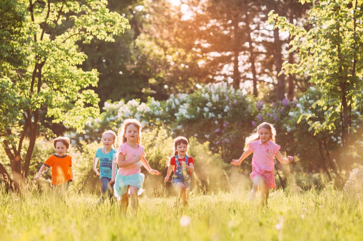 Children running through a sunlit grassy meadow at golden hour